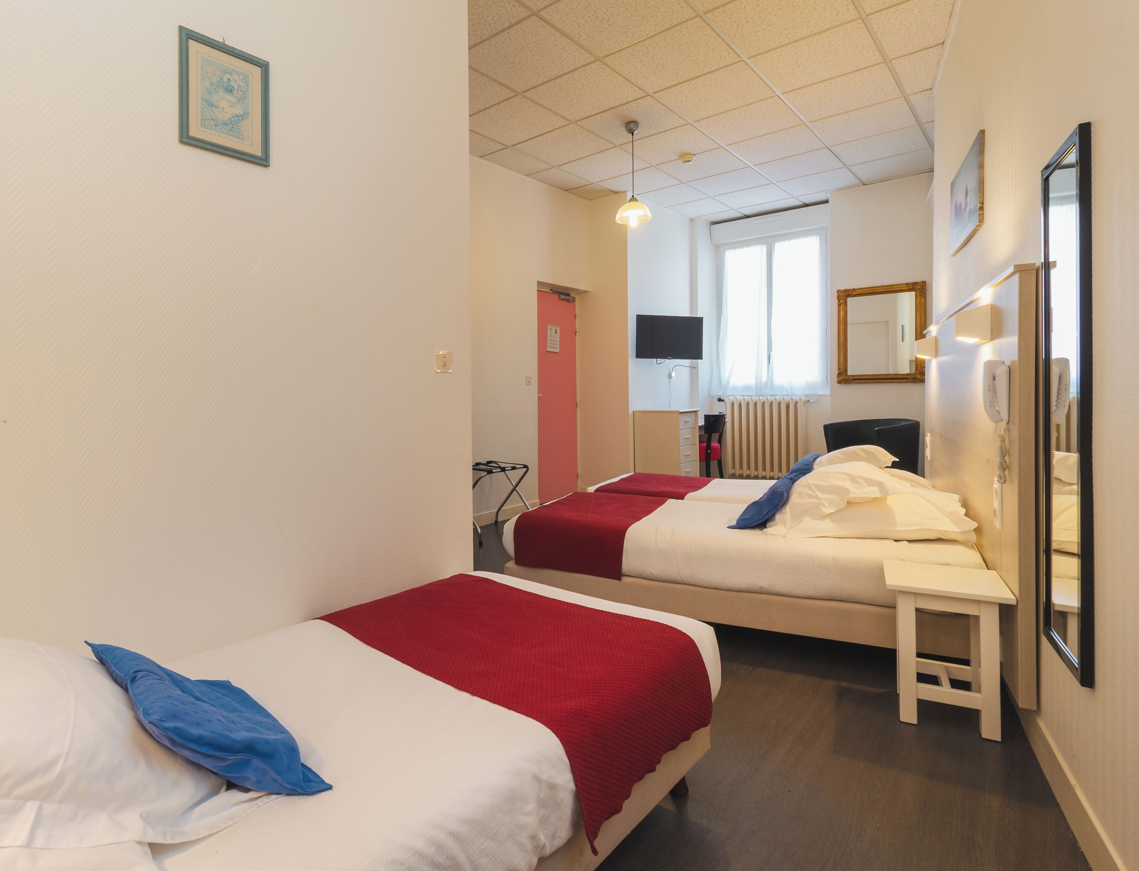 A hotel room with two beds, a TV, a mirror, and a telephone.
