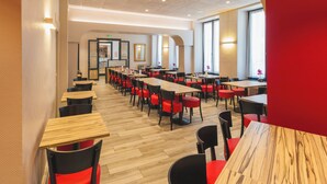 Un vaste espace de restauration dans l’hôtel, avec de nombreuses tables et chaises, un plancher en bois et de grandes fenêtres laissant entrer la lumière naturelle.