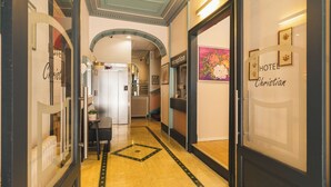 Un hall d’hôtel comprenant un comptoir d’accueil, un espace d’attente avec des chaises et un escalier menant aux étages supérieurs.