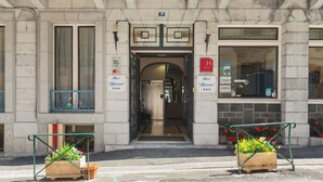 Une entrée d’immeuble avec une porte double, une enseigne indiquant qu’il s’agit d’un hôtel, et deux jardinières ornées de fleurs.