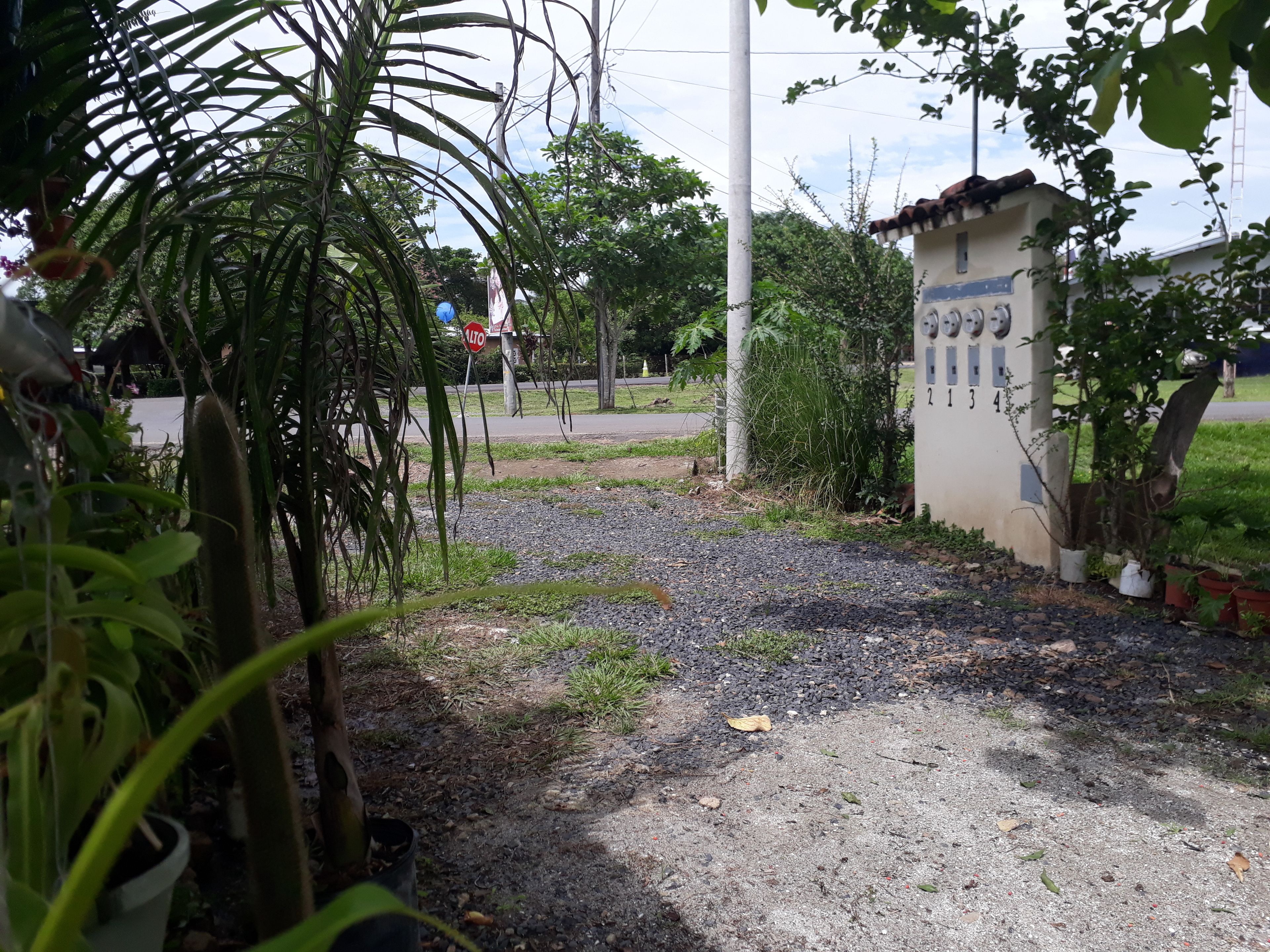 Un chemin de gravier mène à un bâtiment dont les portes sont numérotées, le tout étant entouré de verdure et agrémenté d’un panneau de signalisation.