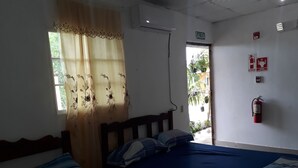 Un dormitorio con dos camas, una ventana con cortinas florales, una puerta que da al exterior y un extintor en la pared.