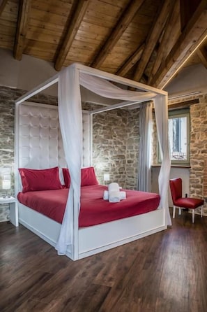 A four-poster bed with a canopy, red bedding, and a stone wall backdrop.