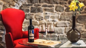 A glass table with a wine bottle, two wine glasses, and a vase with yellow flowers against a stone wall backdrop. - Albergo del Bramante (Roccaverano)