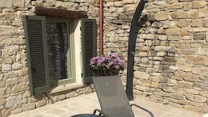 A stone building with a window and shutters, a metal chair, a small round table, and a flower arrangement. - Albergo del Bramante (Roccaverano)