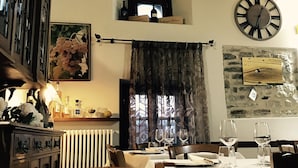 A dining area with wooden beams, a clock, and a stone wall. - Albergo del Bramante (Roccaverano)