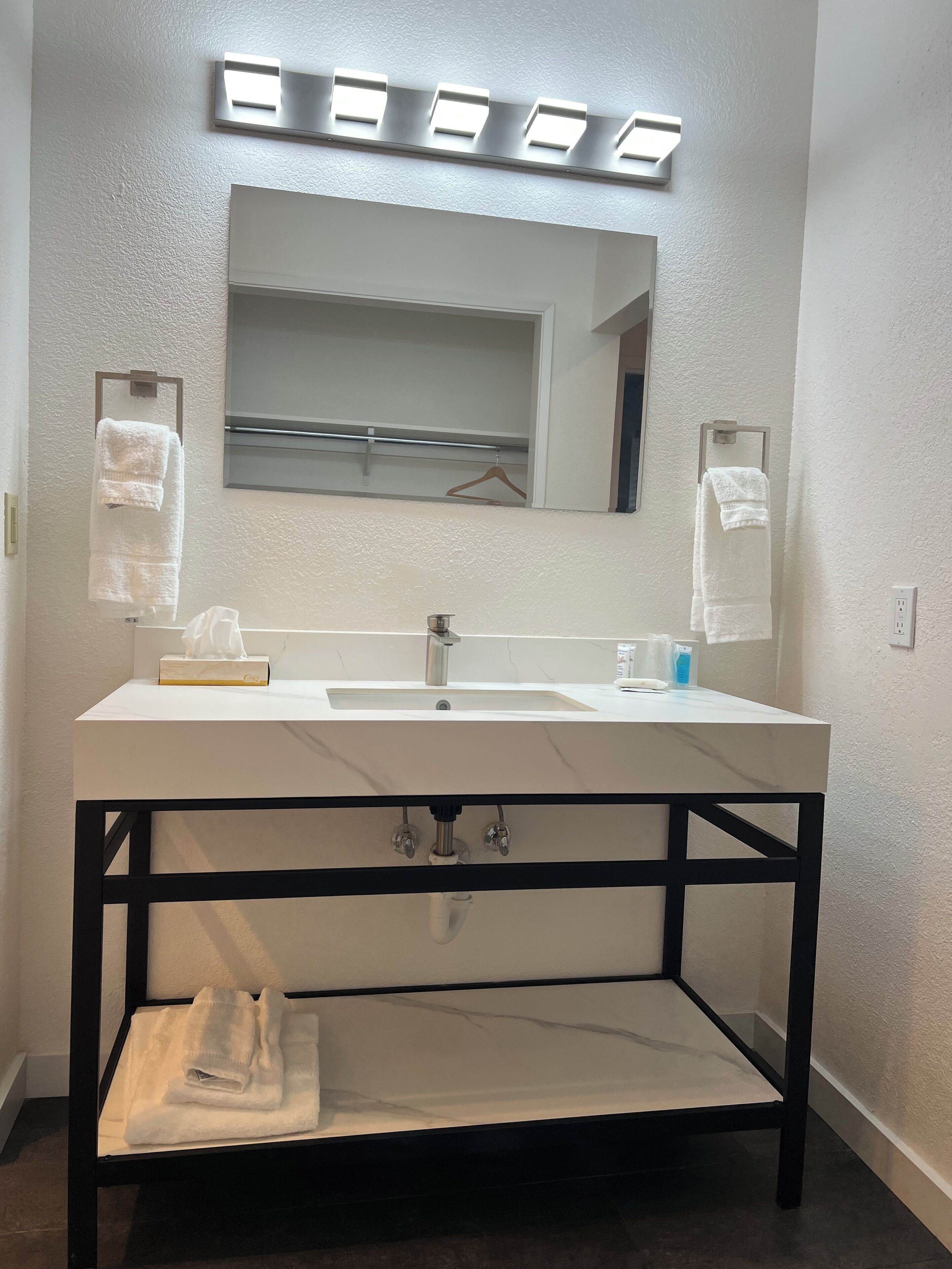 Une salle de bain moderne avec un lavabo blanc, un miroir au-dessus et deux distributeurs de serviettes.