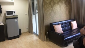 Ein Wohnzimmer mit einer schwarzen Ledersofa, einer kleinen Küchenzeile inklusive Mikrowelle und einer Glastür, die auf einen Balkon führt.