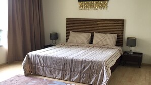 Ein Schlafzimmer mit einem großen Bett, zwei Nachttischen, einem Wandbild und einem gemusterten Teppich.