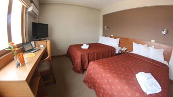 A hotel room with two beds, a desk with a laptop, a television, and a window with curtains.