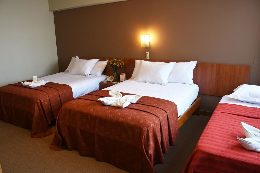 A hotel room with two single beds, a wooden headboard, a nightstand with a phone, and a wall-mounted light.