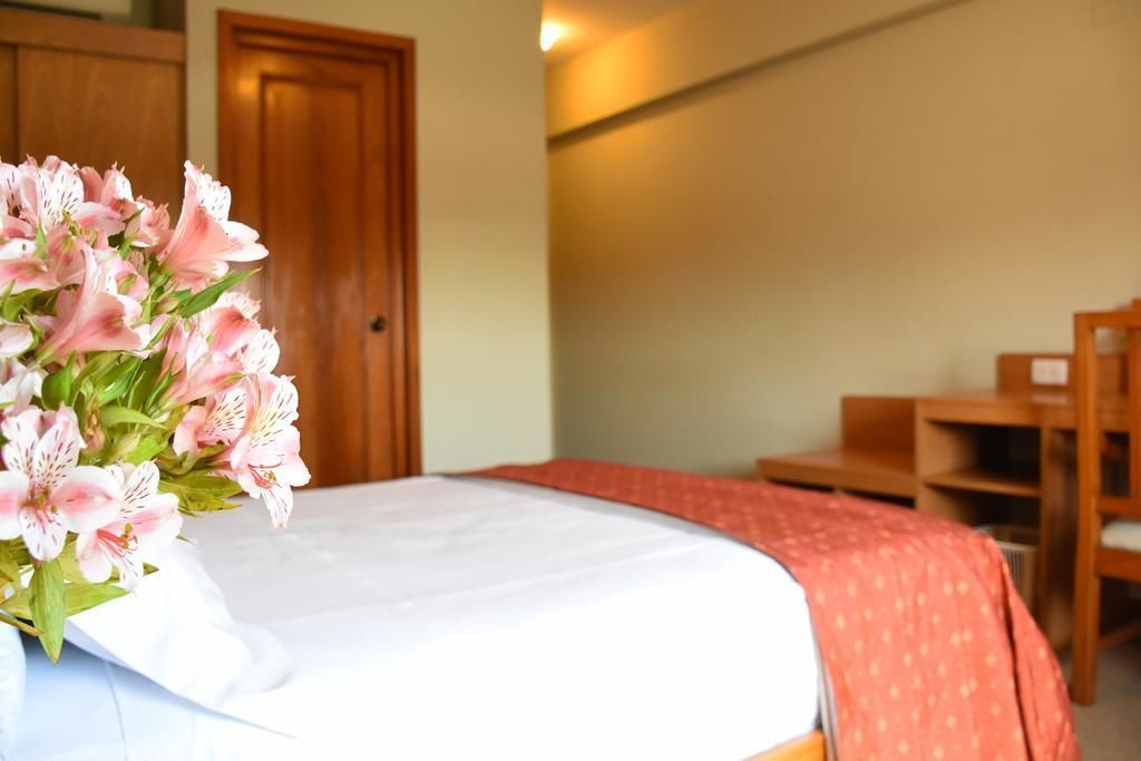 A neatly made bed with a white sheet and a pink floral arrangement on the left side.