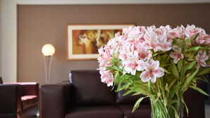 A bouquet of pink flowers in a vase on a table in a room with a brown leather couch and a framed painting on the wall. - Hotel Paraiso Trujillo (Trujillo)