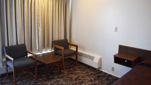 A room with a sofa, two chairs, a small table, a heater, and a window with curtains.