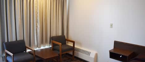 A room with a sofa, two chairs, a small table, a heater, and a window with curtains.