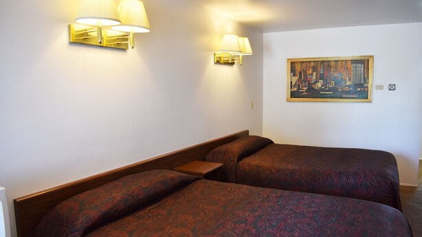 A hotel room with two beds, each with a patterned bedspread, two wall-mounted lamps, and a framed painting on the wall.