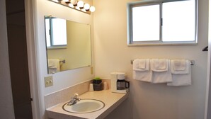 A bathroom with a sink, mirror, and window. There are towels hanging on the wall and a coffee maker on the counter.
