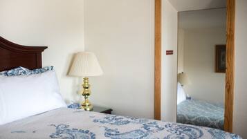 A neatly made bed with a patterned bedspread, a bedside lamp, and a mirror reflecting another room.