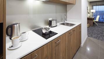 A modern kitchen with a coffee maker, kettle, and toaster, a sink, and wooden cabinets.
