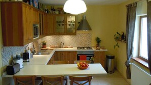 A kitchen with wooden cabinets, a central island, a gas stove, and a sink. - Belegania (Oarja)
