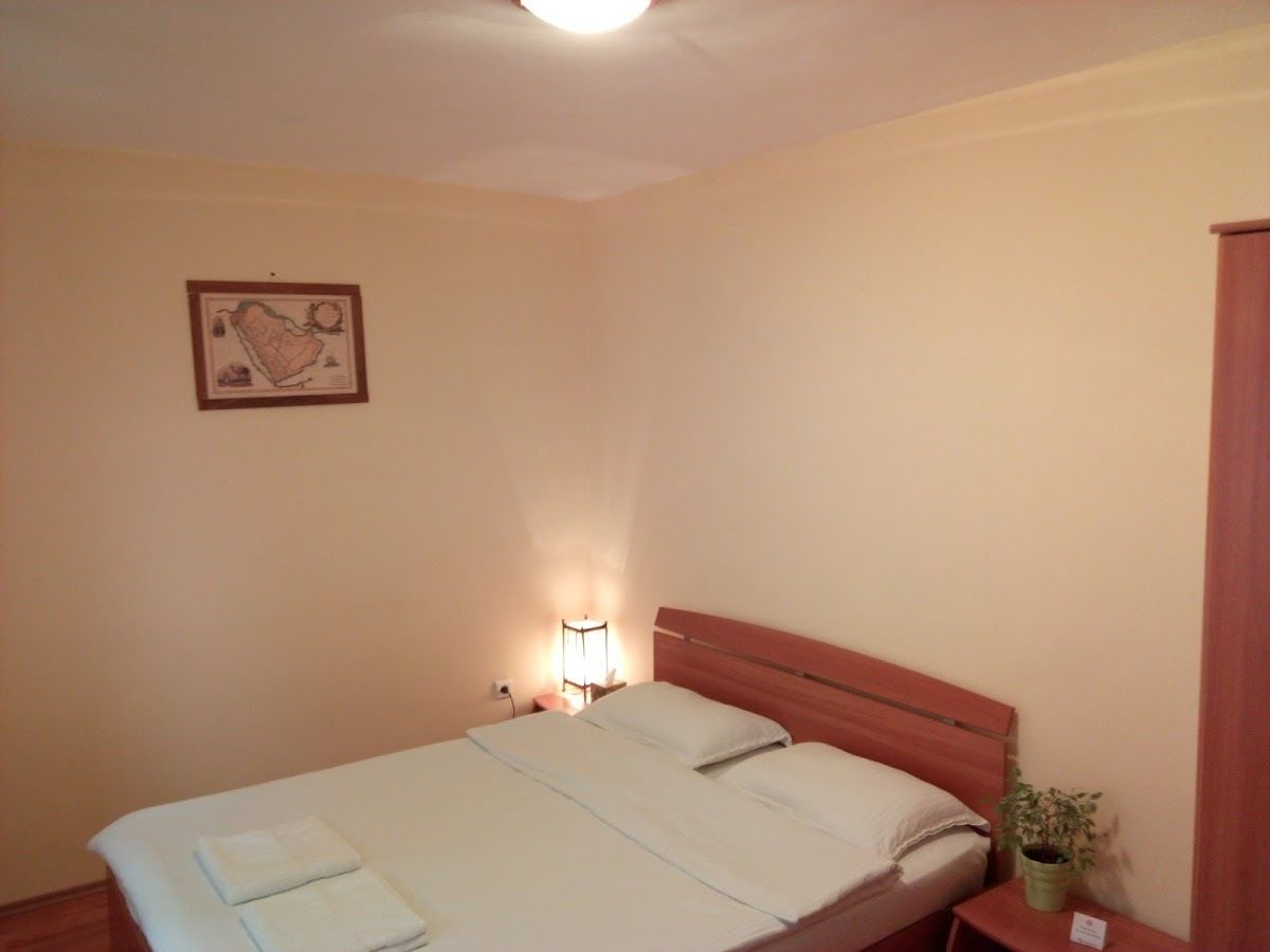 A bedroom with a single bed, a bedside lamp, a framed picture on the wall, and a small table with a plant.