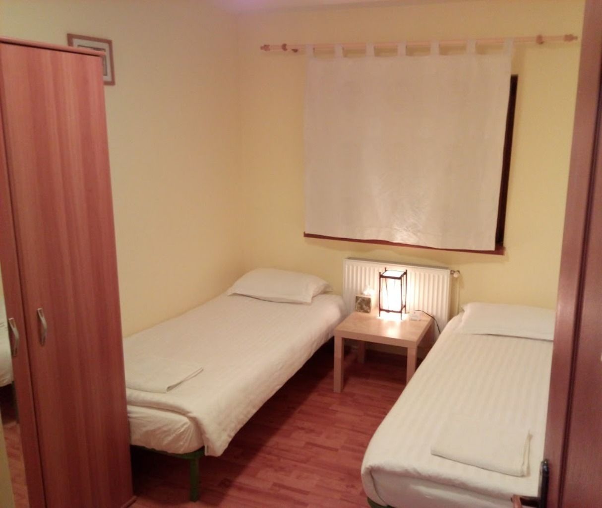 A small room with two single beds, a wooden nightstand, and a radiator.