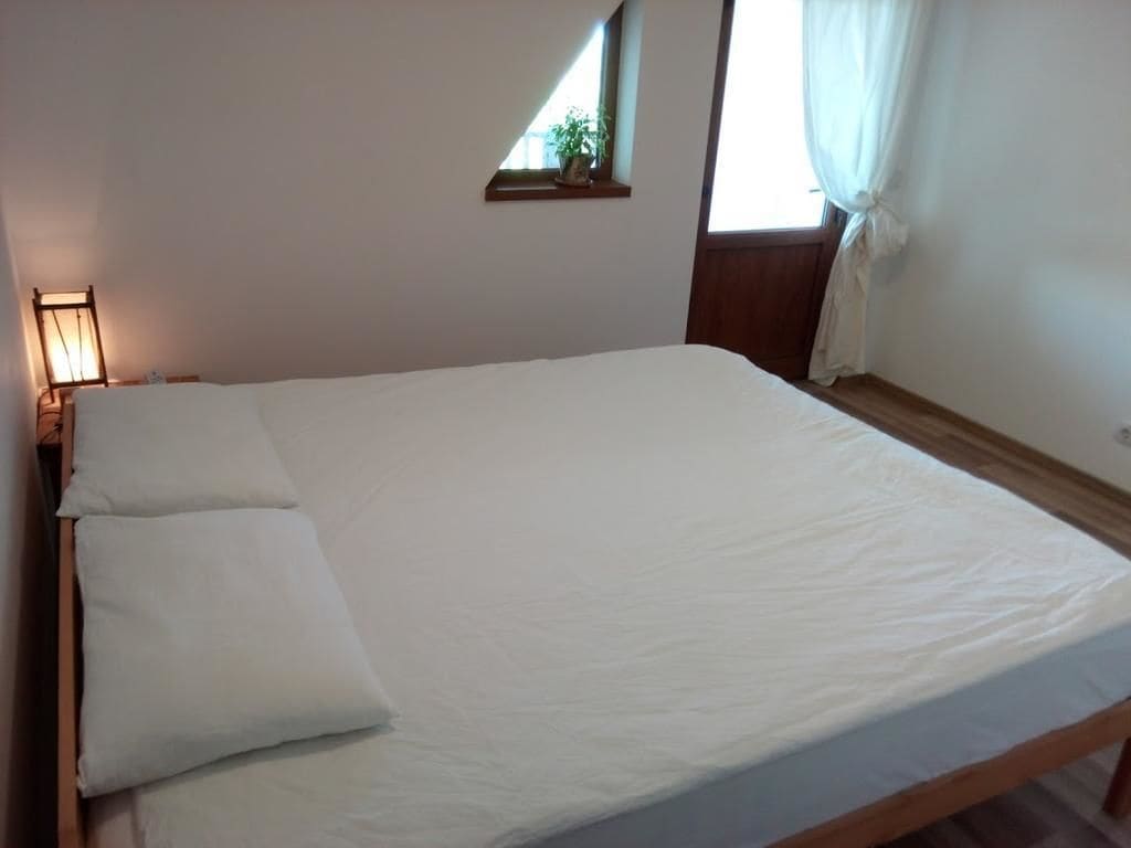 A single bed with white bedding in a room with a sloped ceiling and a small window with curtains.