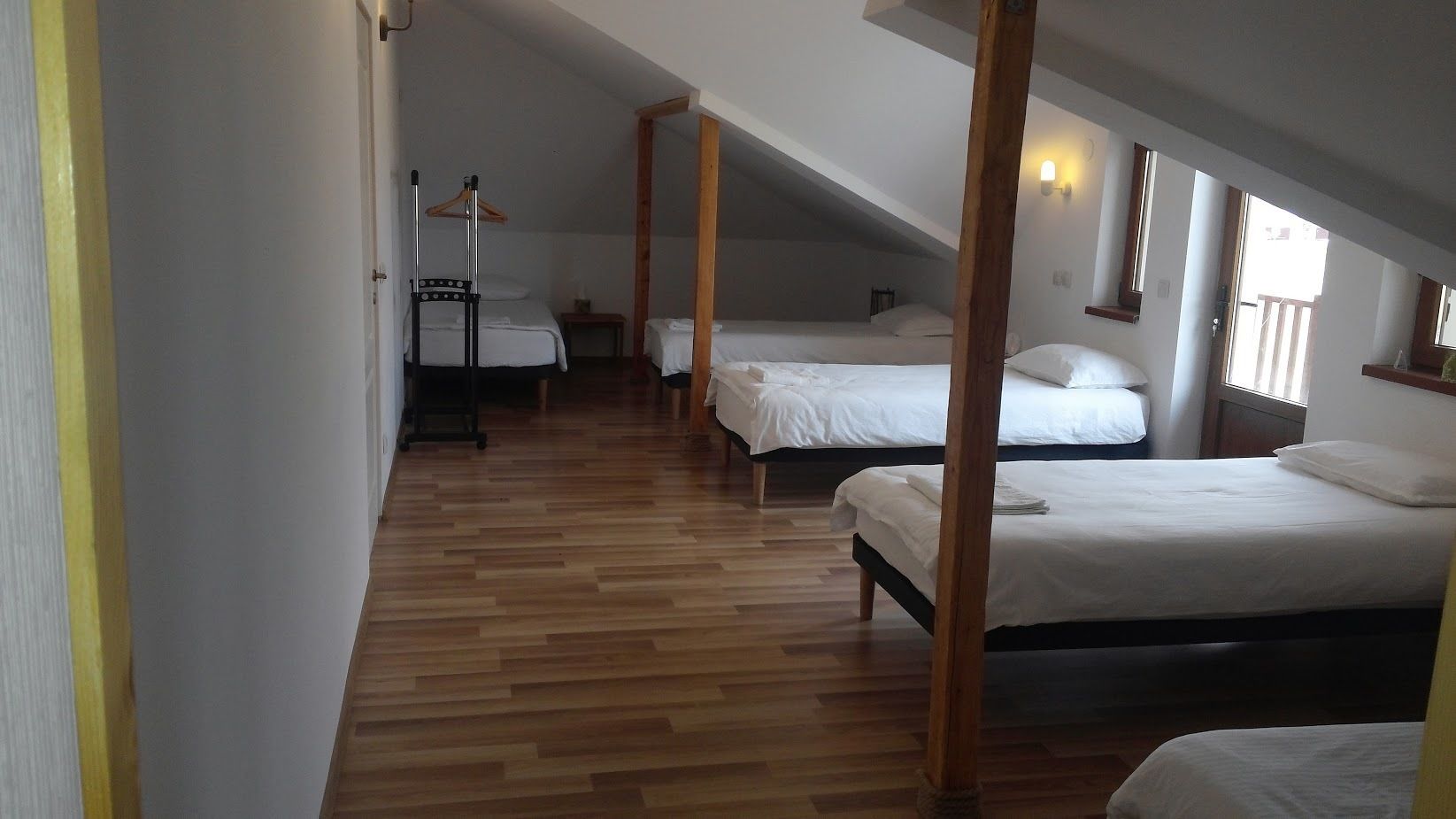 A dormitory-style room with wooden flooring, multiple beds, and a wooden ceiling structure.