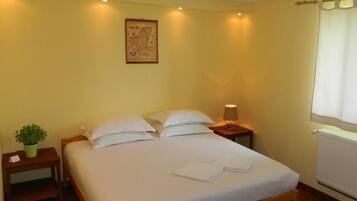 A bedroom with a single bed, a nightstand with a lamp, a potted plant, and a map on the wall.