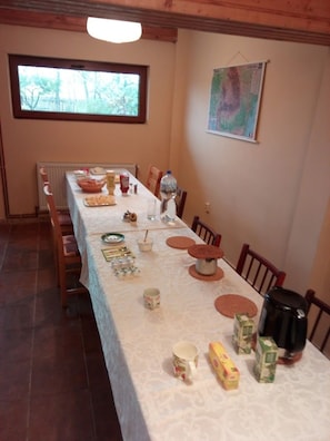 A dining area with a long table set for a meal, chairs, a window, and a map on the wall.