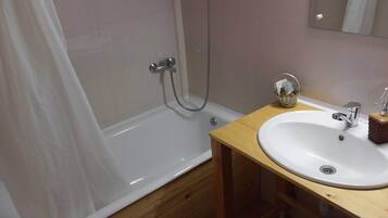 Un baño con una bañera blanca, un tocador de madera con un lavabo y un espejo sobre el lavabo.