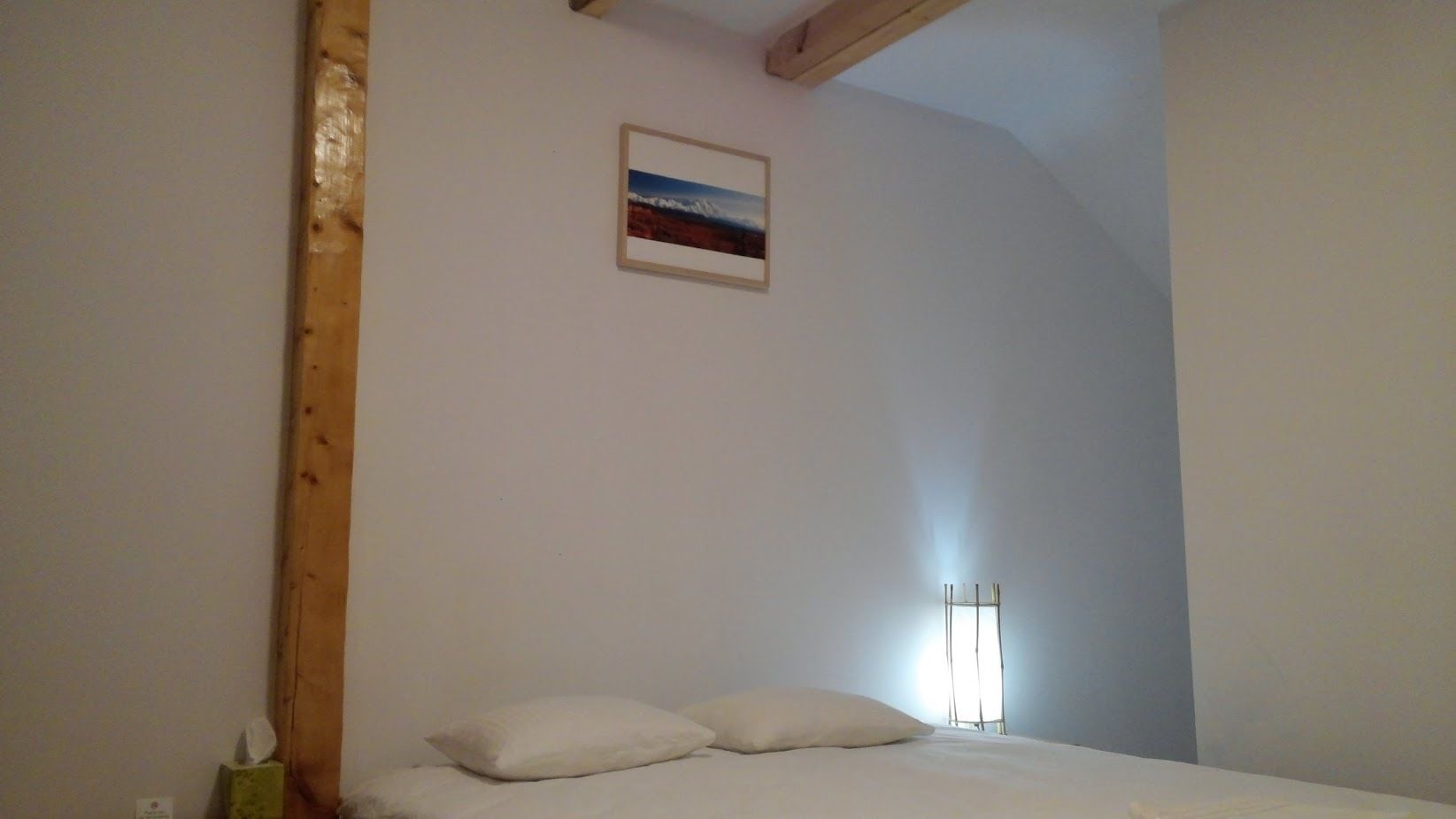 Un dormitorio con cama, almohadas, un cuadro pequeño en la pared y una lámpara de pie alta.