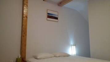 Un dormitorio con cama, almohadas, un cuadro pequeño en la pared y una lámpara de pie alta.