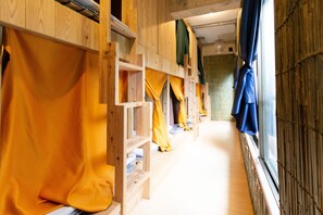 Une rangée de lits superposés en bois, avec des rideaux jaunes et bleus, un sol carrelé et une fenêtre ornée de stores en bambou.