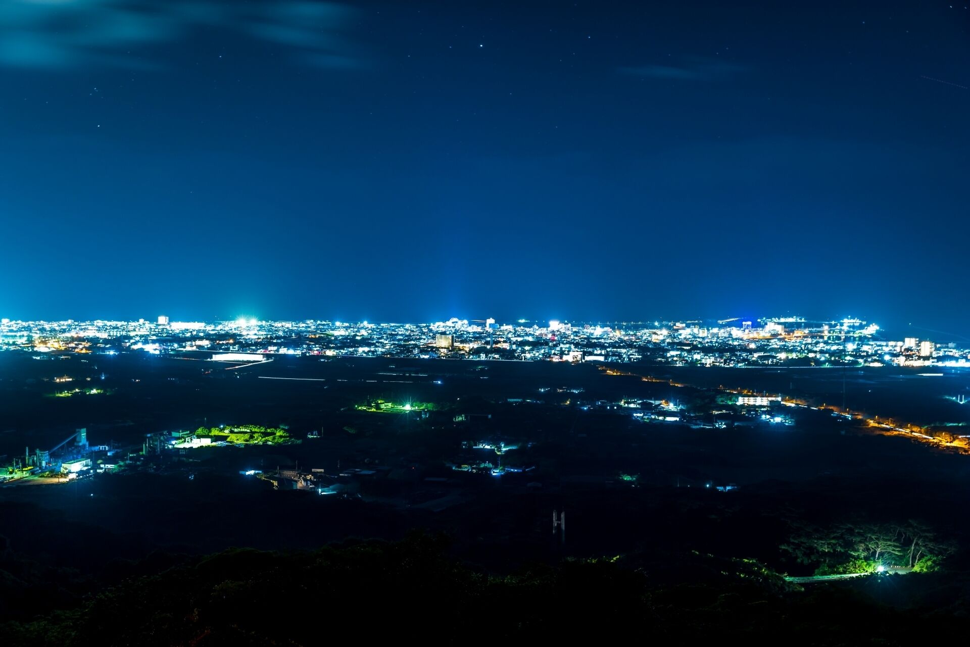 Une vue nocturne d’une ville, avec en arrière-plan une zone densément peuplée illuminée par de nombreuses lumières.