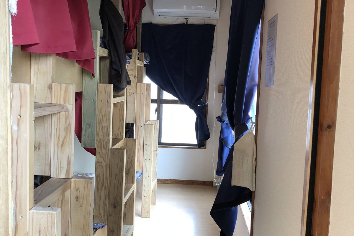 Une petite pièce avec des lits superposés en bois, un ventilateur de plafond, un appareil de climatisation et une fenêtre avec des rideaux.