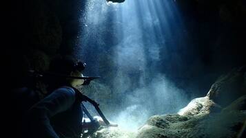 A person in scuba gear inside a cave with sunlight streaming through an opening.