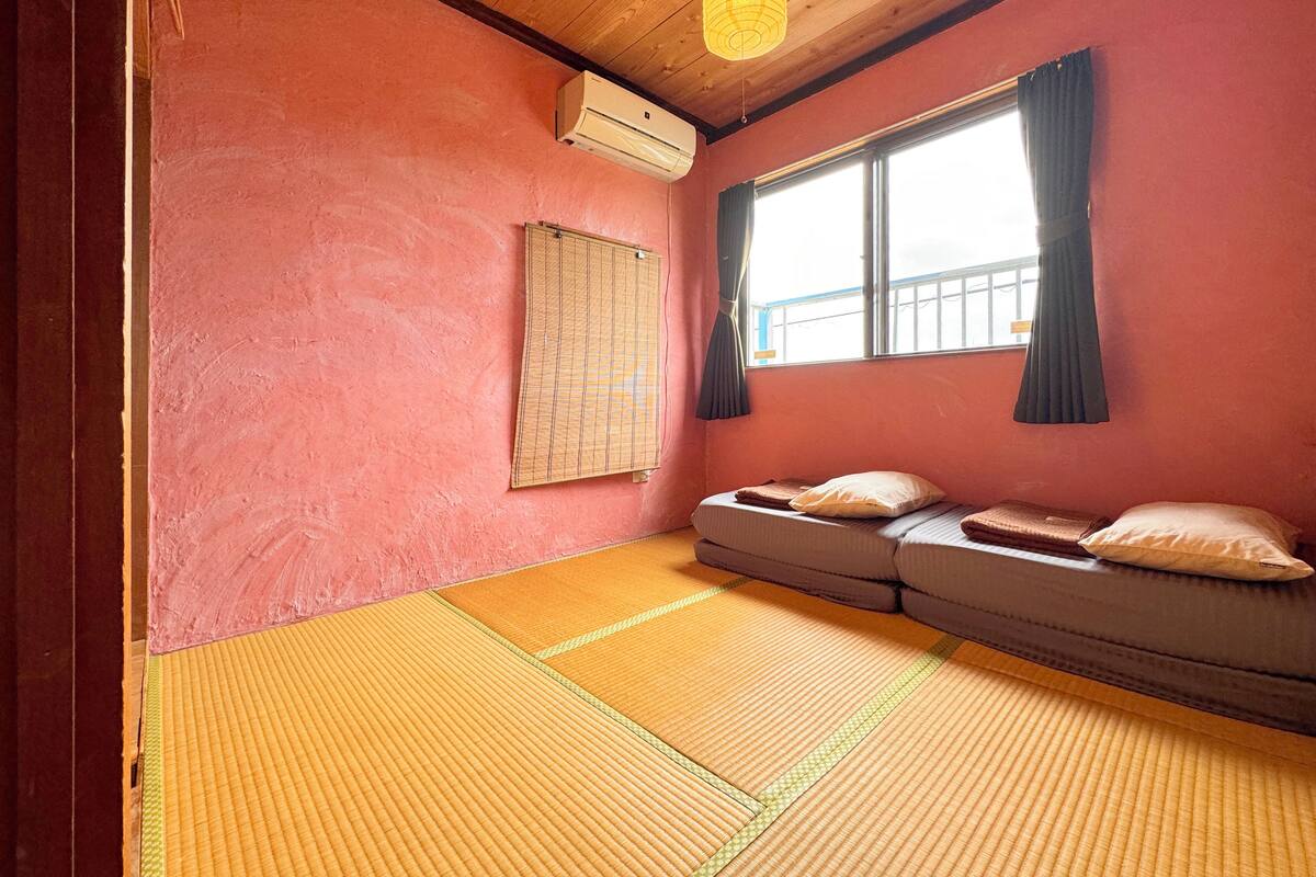 Une pièce avec des tatamis, un futon, une fenêtre avec des rideaux et un appareil de climatisation.