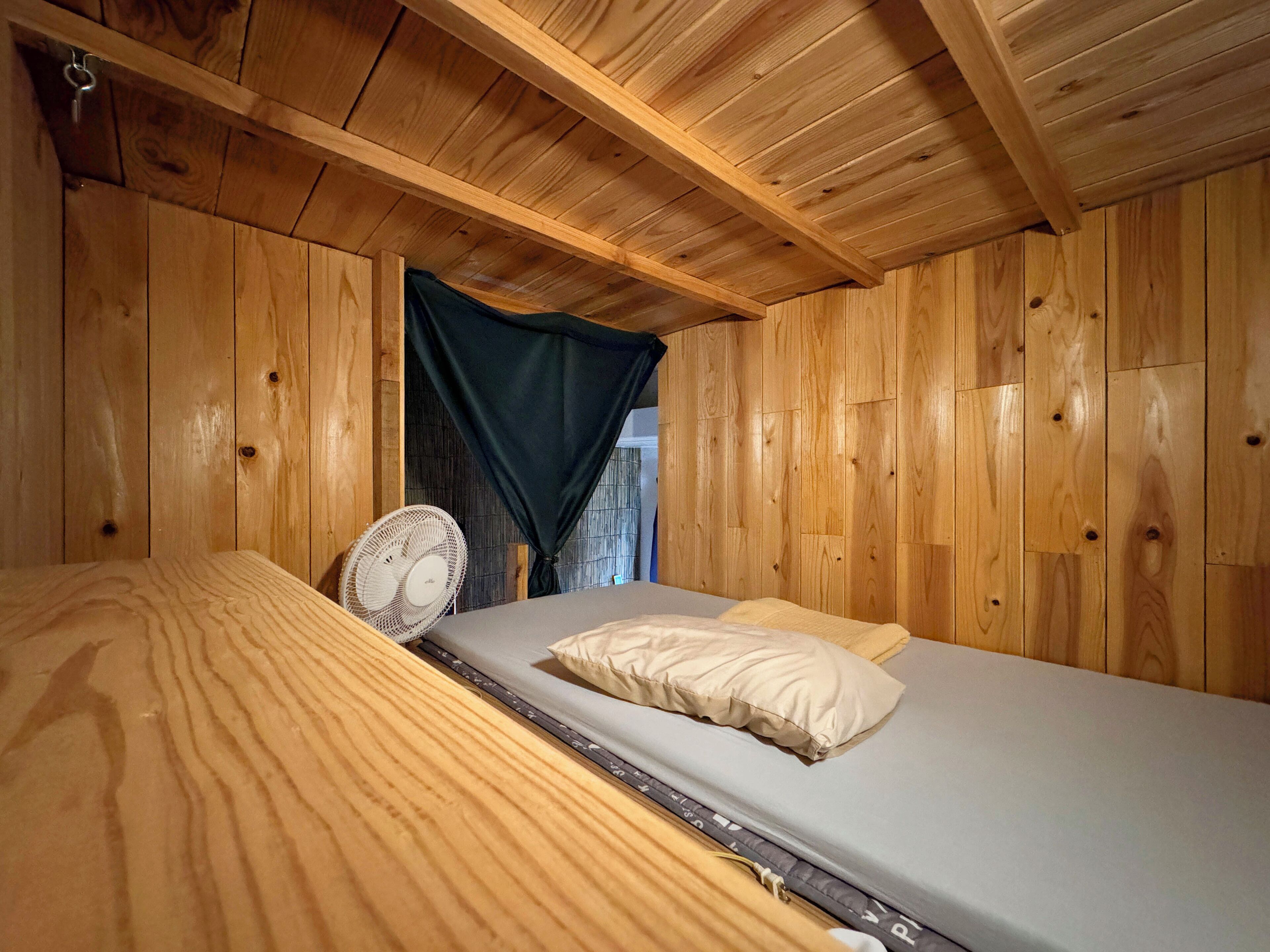 A wooden cabin room with a bed, a fan, and a curtain.