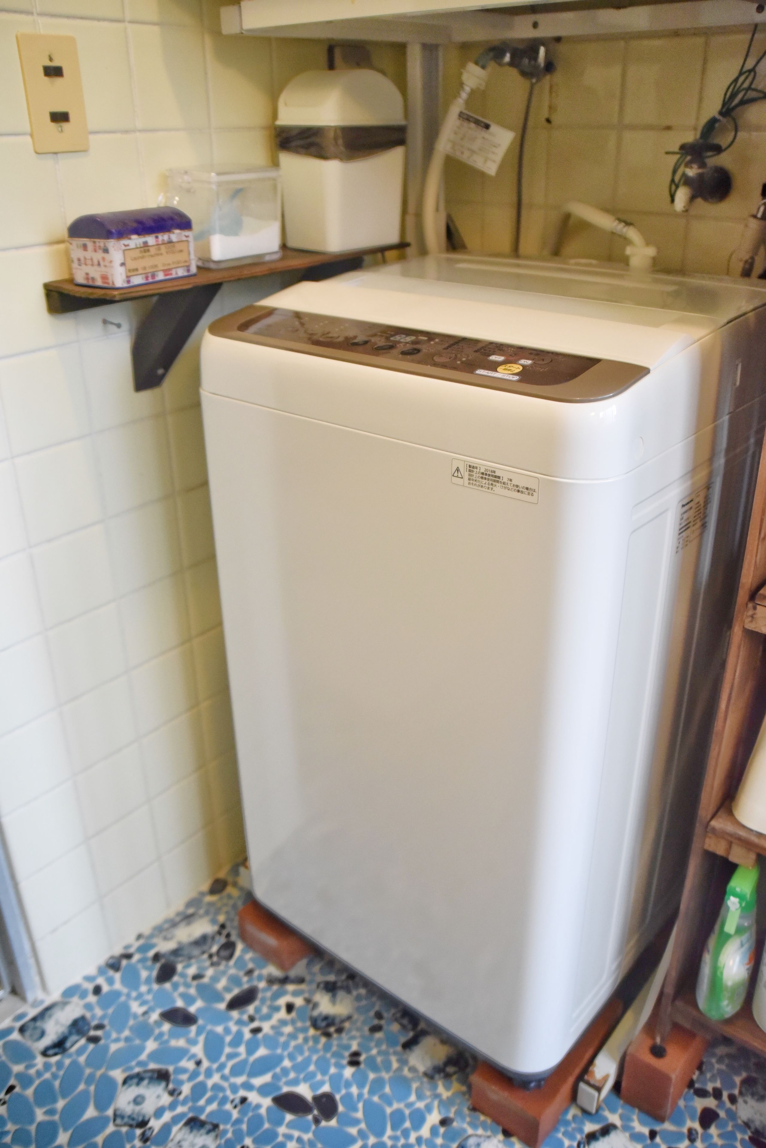 A compact refrigerator with a control panel, situated in a kitchen with a tiled backsplash and a blue speckled floor.