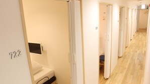 A hotel corridor with wooden flooring, white walls, and numbered doors. - Executive Spa & Capsule WELLBE Fukuoka - Caters to Men (Fukuoka)