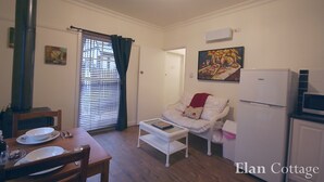 A cozy living room with a dining table set, a white sofa, a small white table, a white refrigerator, and a chimney.