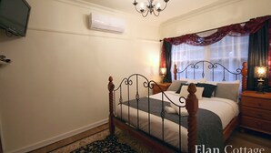 A bedroom with a four-poster bed, a chandelier, a flat-screen TV mounted on the wall, and a window with red curtains.