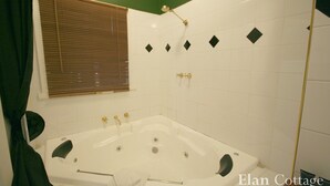 A bathroom with a large bathtub, a shower area, and a window with blinds.