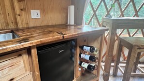 Una cocina de madera con lavavajillas integrado, botellas de vino en una estantería y vistas a través de una ventana con celosía.