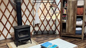 Una habitación acogedora con un armario de madera, una mesita con libros, una estufa negra y una alfombra colorida.