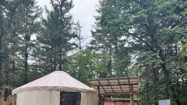 Un camping con una tienda de campaña grande, una mesa de picnic de madera y un área de estar cubierta.