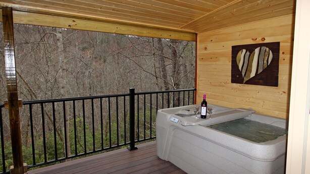 Eine Holzhütte mit Whirlpool, einer Weinflasche und einem Glas auf der Terrasse.