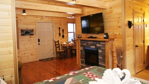 Ein gemütliches Blockhaus mit Holzwänden, einem Kamin, einem darüber montierten Fernseher und einer Decke auf dem Boden.
