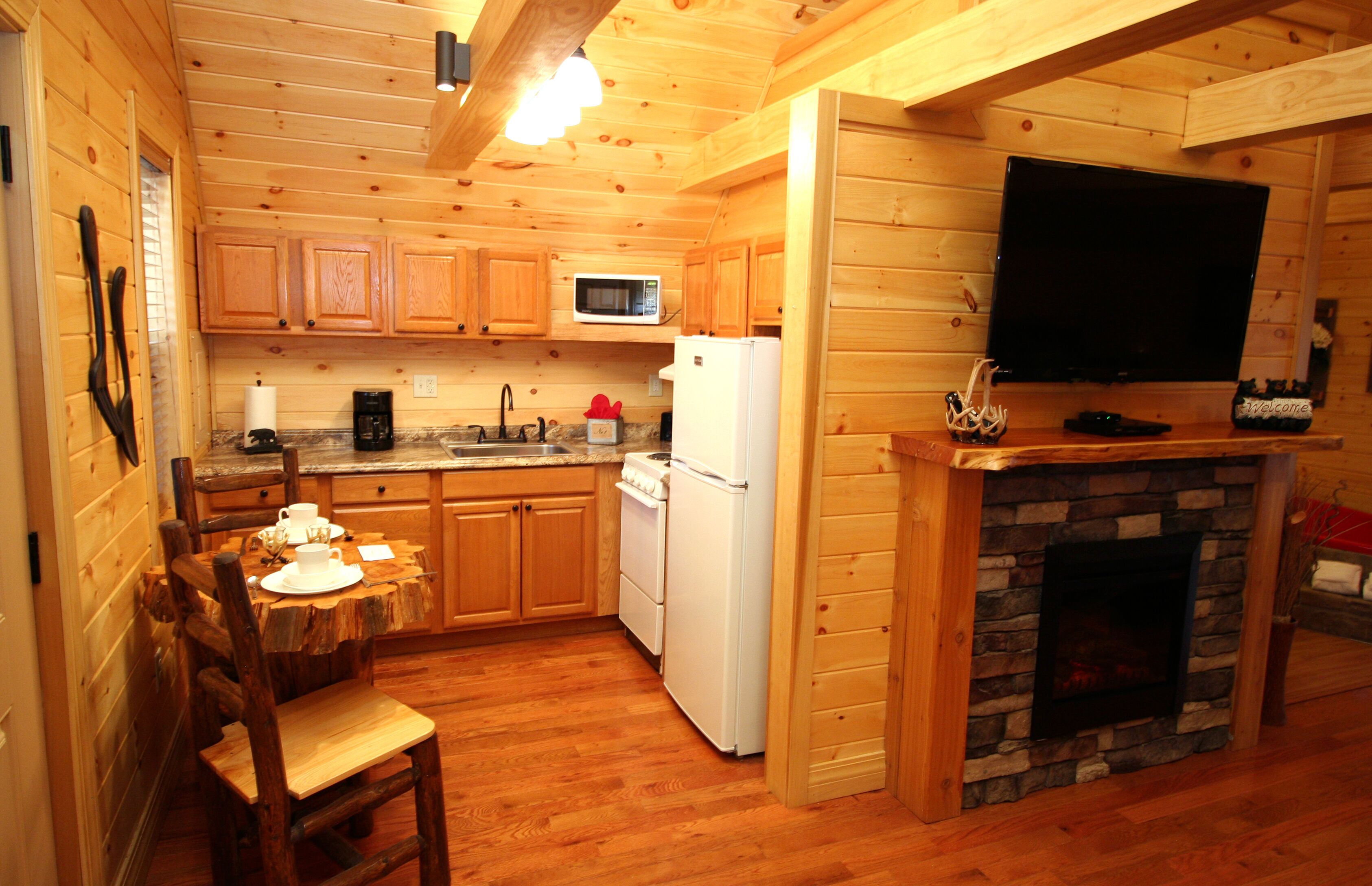 A wooden cabin-style kitchen with wooden cabinets, a stone fireplace, a microwave, and a television mounted above the fireplace.